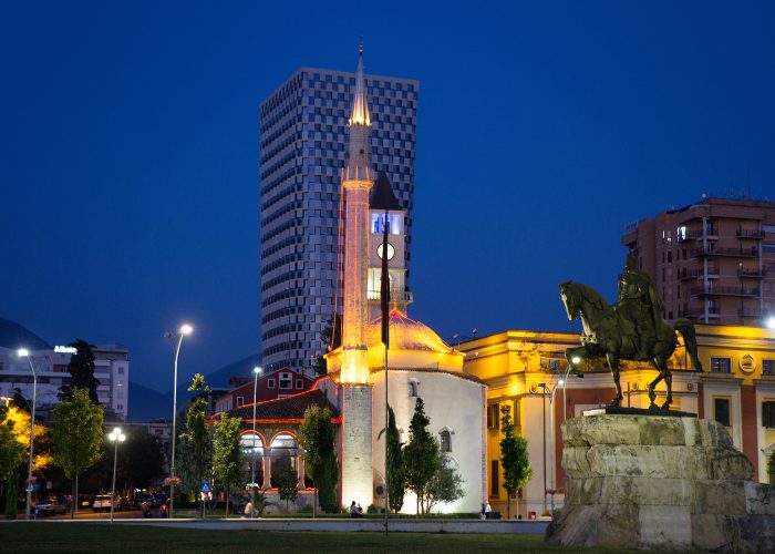 The illuminated Skanderbeg Square at Tirana, Albania at night with Et'hem Bey Mosque and a modern office building in the background