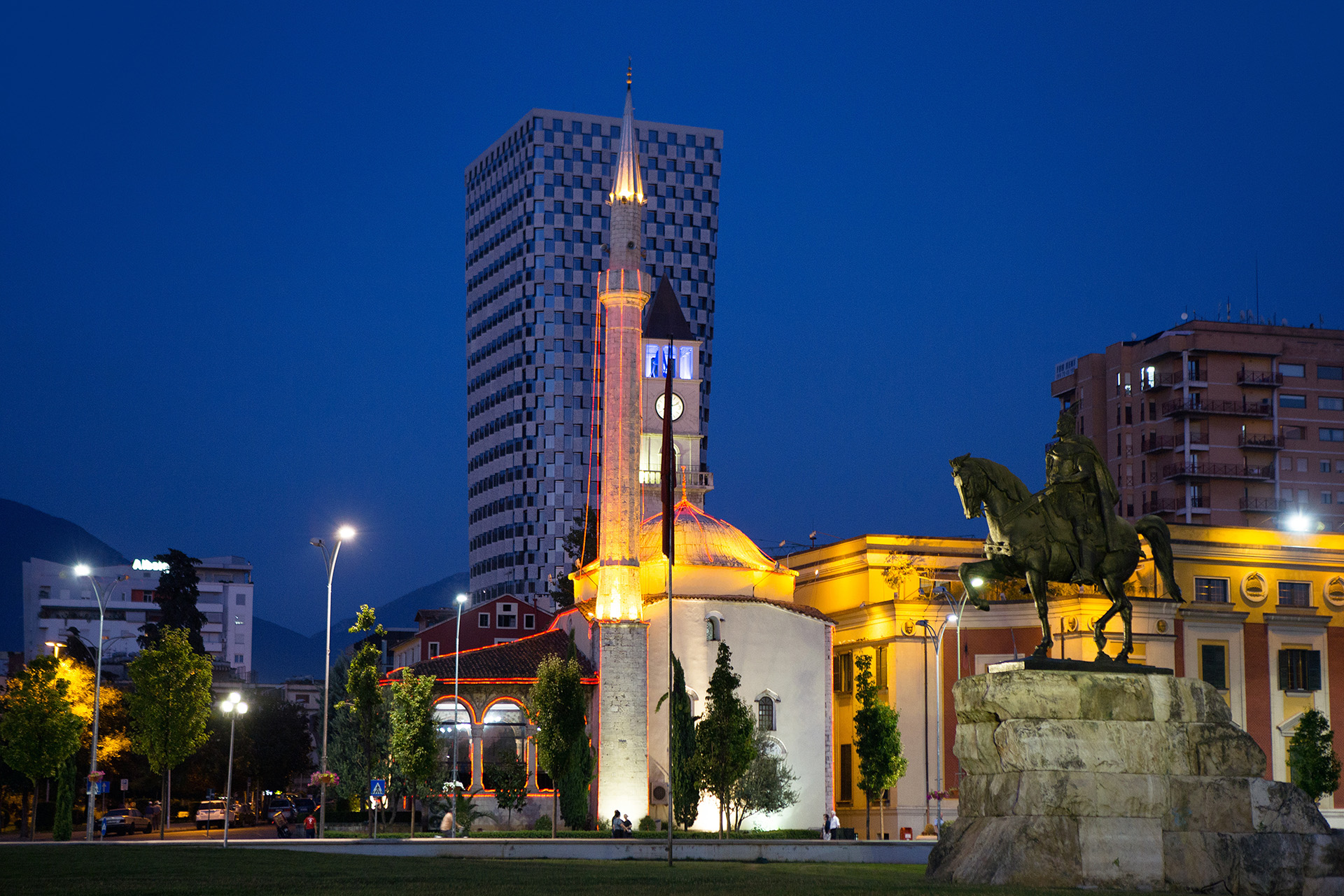 The illuminated Skanderbeg Square at Tirana, Albania at night with Et'hem Bey Mosque and a modern office building in the background